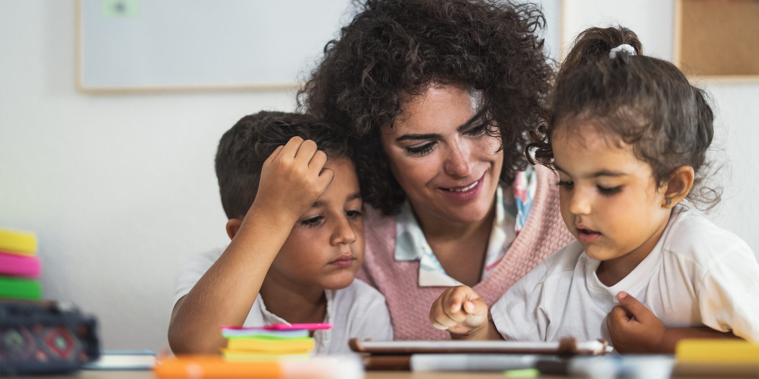 Teacher with children using digital tablet in preschool classroom - Education and technology concept